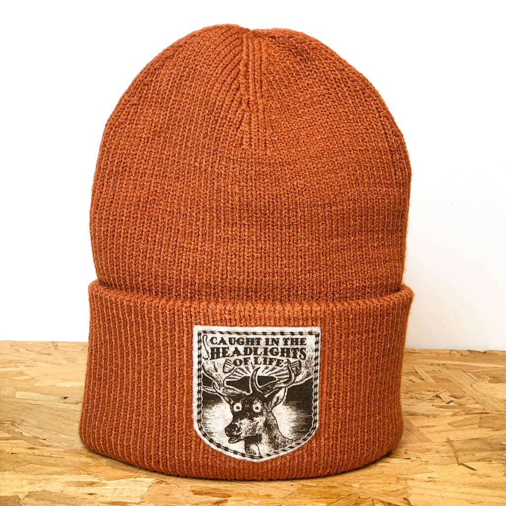 Caught in the Headlights of Life orange deep-cuffed 100% recycled polyester beanie, decorated with wool felt badge hand printed by All’s Well Originals with deer graphic and text 